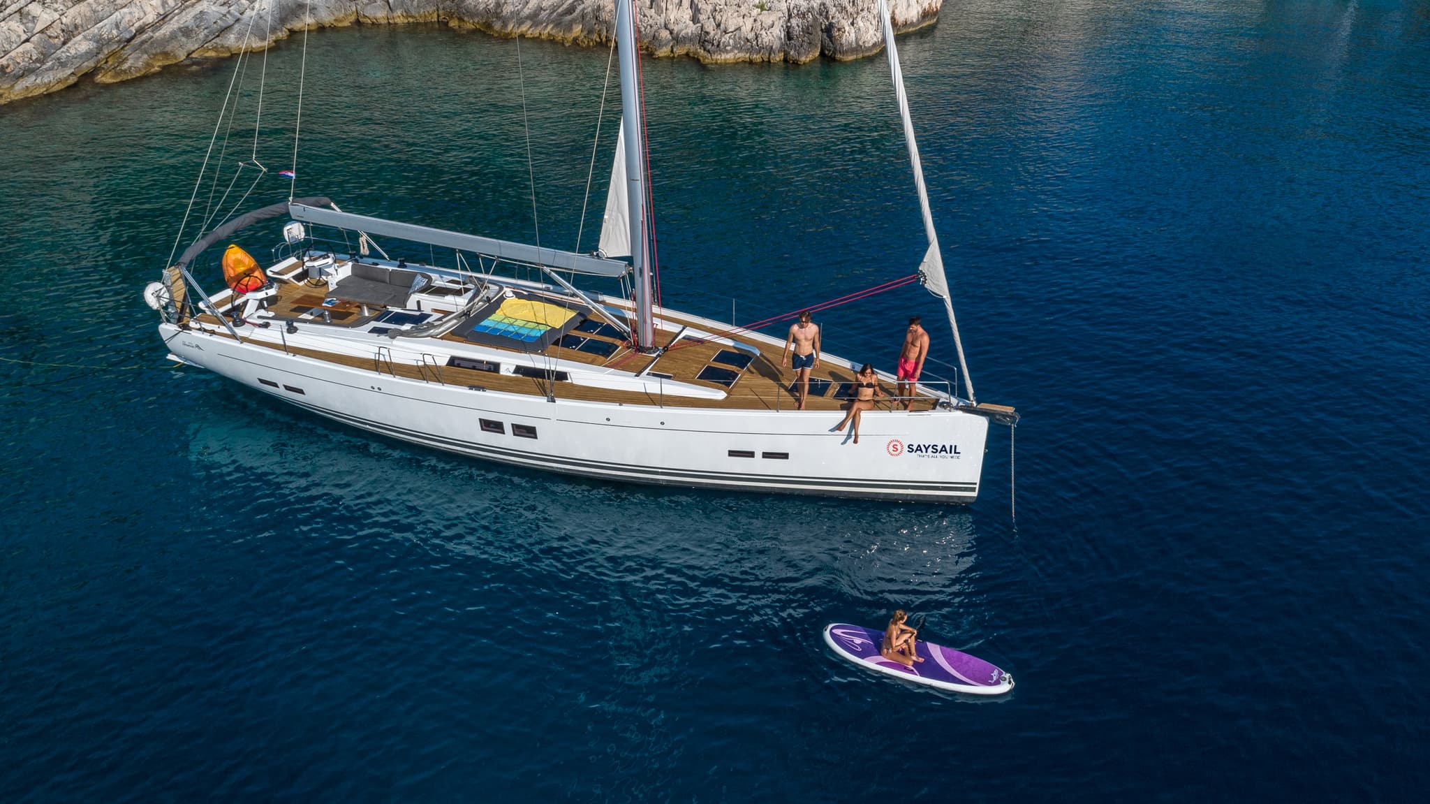 Aerial view of a Hanse sailing yacht on clear water with one person paddleboarding nearby