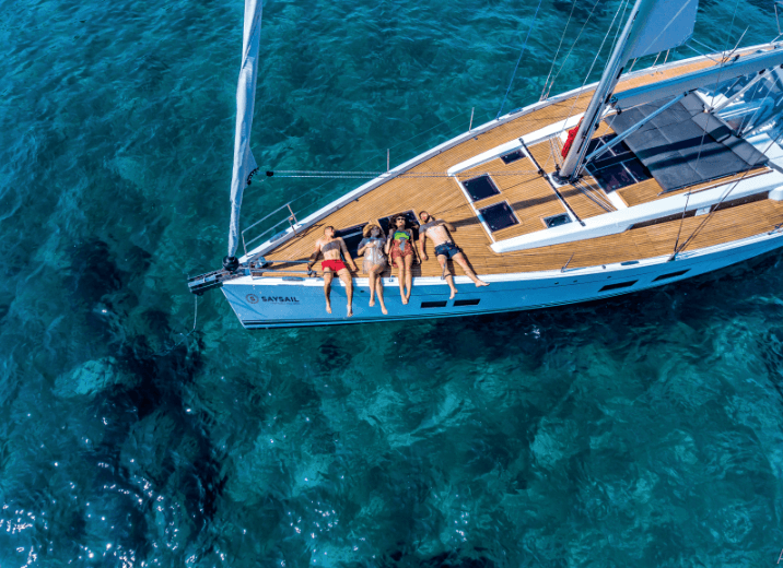 Aerial view of four people sunbathing on the deck of a Hanse sailboat over clear blue waters