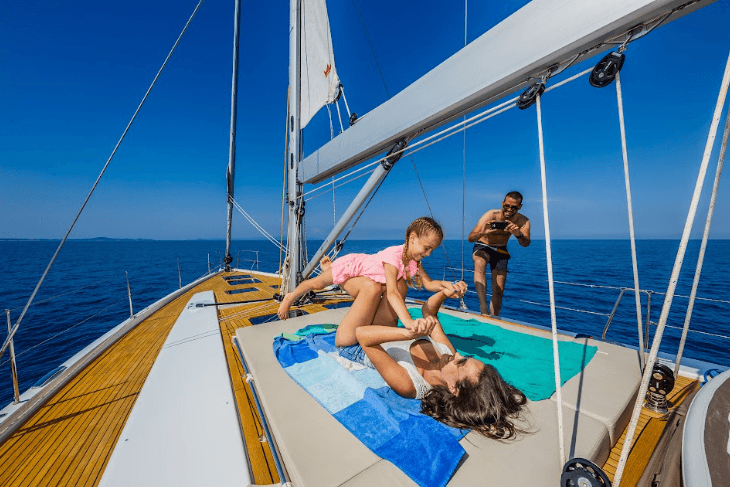 Family playing on a Hanse sailing yacht deck with clear blue skies and calm sea in the background